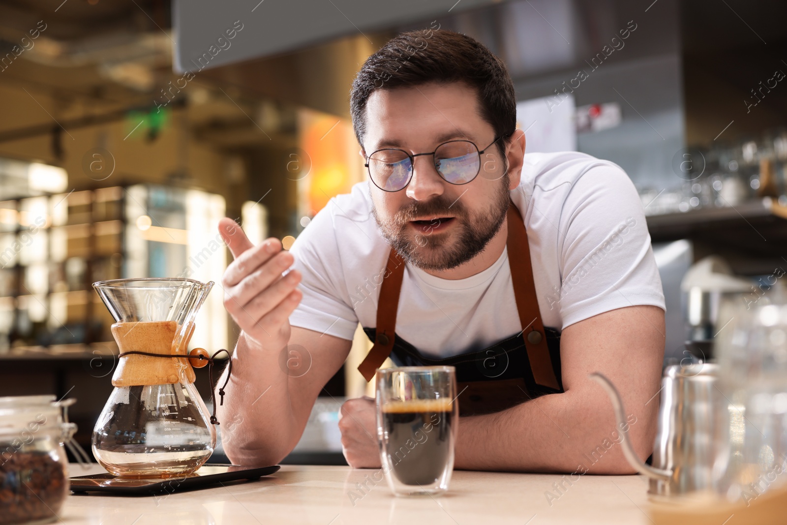 Photo of Barista sniffing aromatic filter coffee at table in cafe