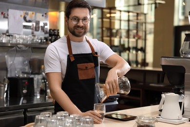 Barista pouring coffee from glass coffeemaker into cup at table in cafe