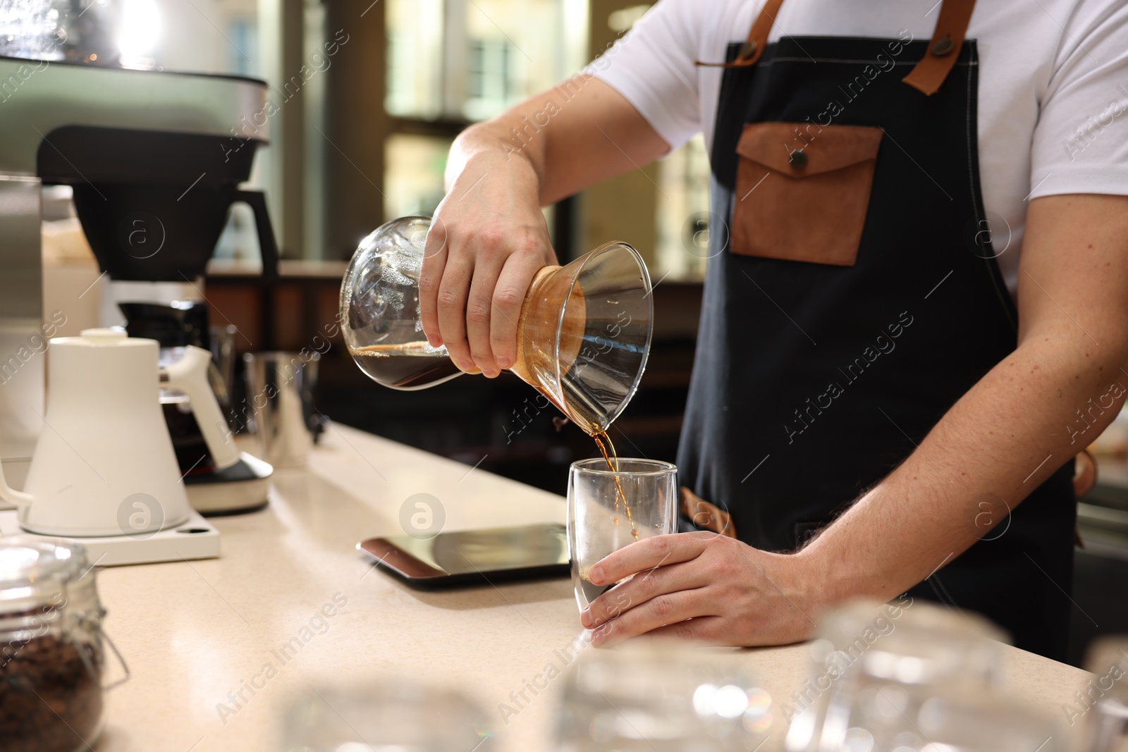 Photo of Barista pouring coffee from glass coffeemaker into cup at table in cafe, closeup