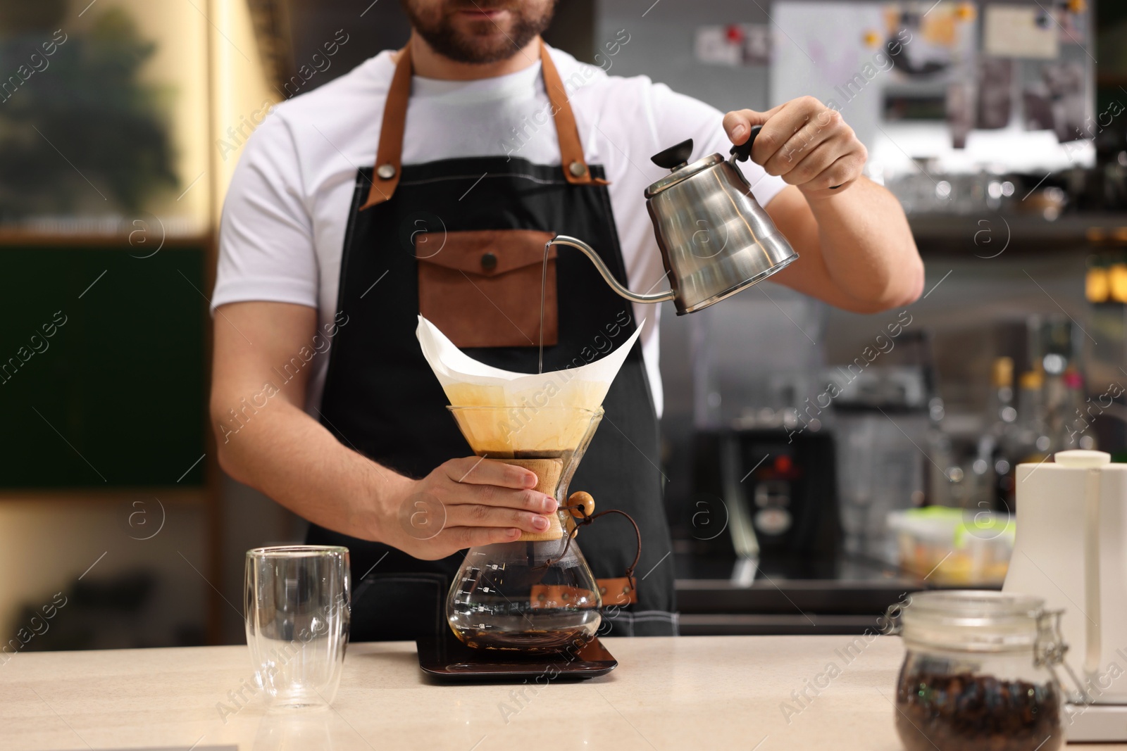 Photo of Barista brewing coffee in glass coffeemaker with paper filter at table in cafe, closeup