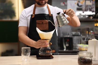 Photo of Barista brewing coffee in glass coffeemaker with paper filter at table in cafe, closeup