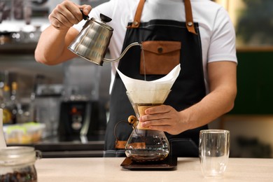 Photo of Barista brewing coffee in glass coffeemaker with paper filter at table in cafe, closeup