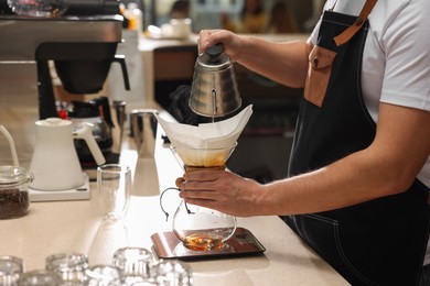 Photo of Barista brewing coffee in glass coffeemaker with paper filter at table in cafe, closeup