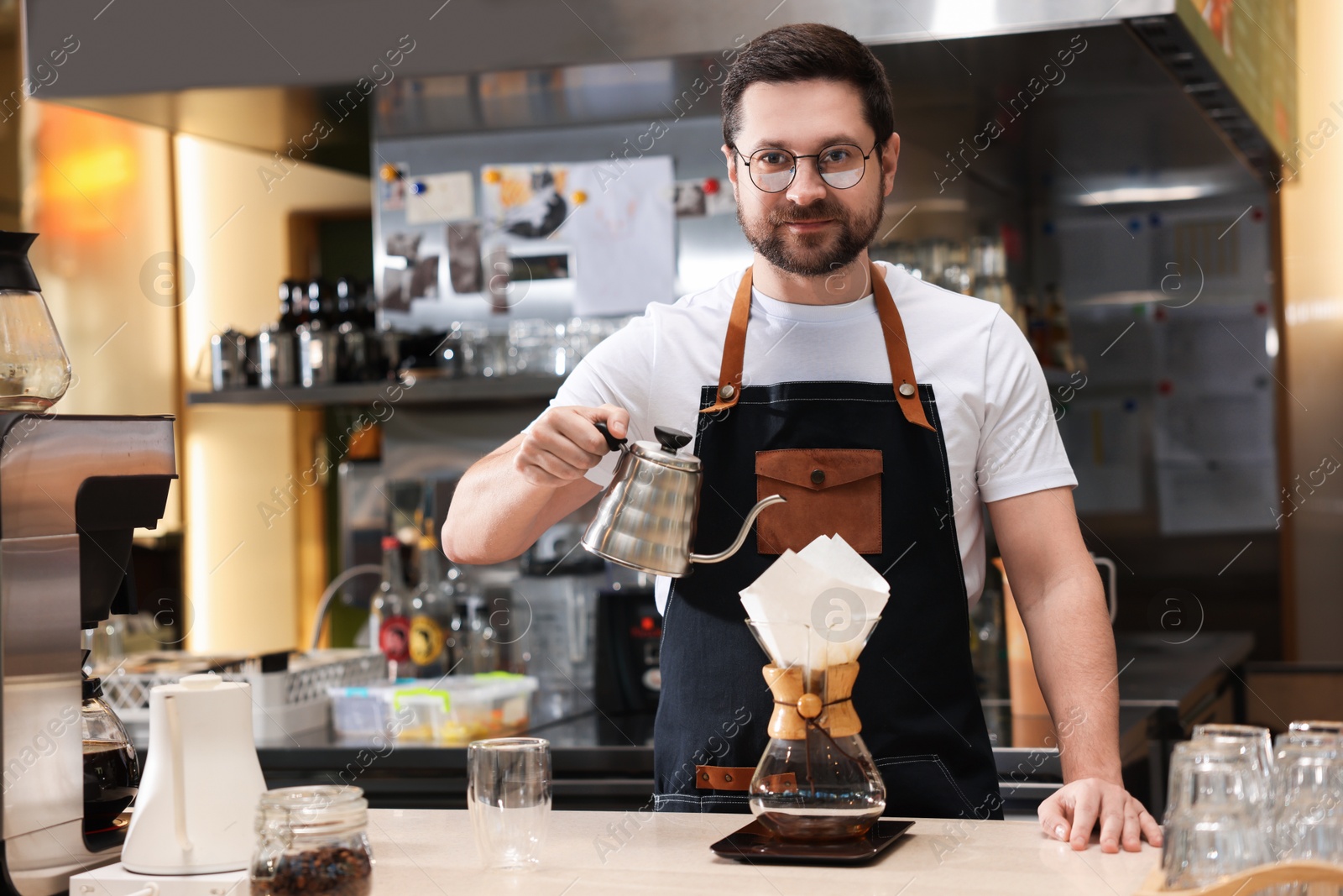 Photo of Barista brewing coffee in glass coffeemaker with paper filter at table in cafe