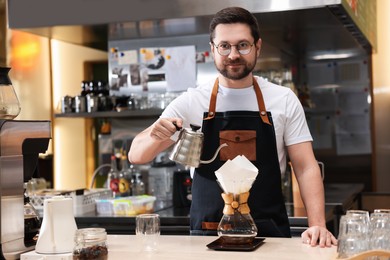 Barista brewing coffee in glass coffeemaker with paper filter at table in cafe