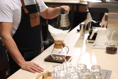 Barista brewing coffee in glass coffeemaker with paper filter at table in cafe, closeup