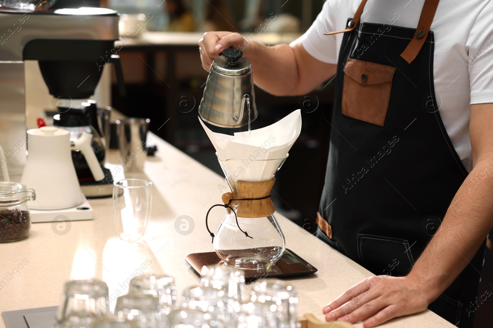 Photo of Barista brewing coffee in glass coffeemaker with paper filter at table in cafe, closeup