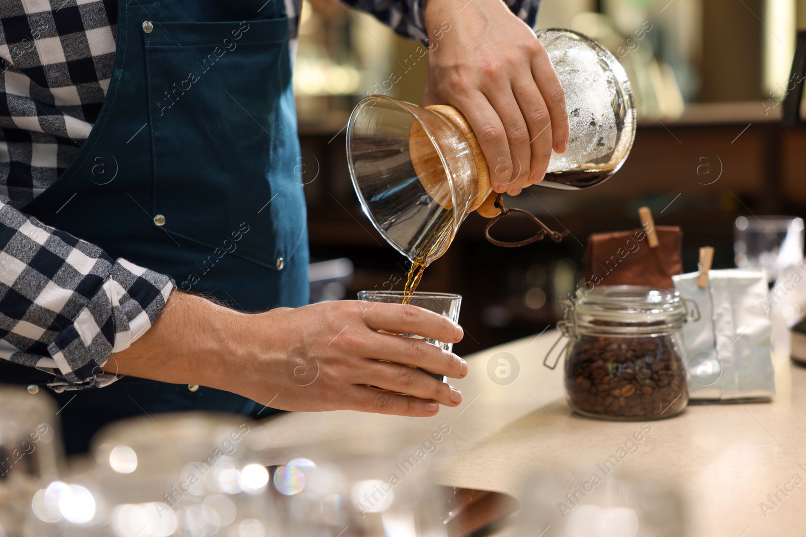 Photo of Barista pouring coffee from glass coffeemaker into cup at table in cafe, closeup