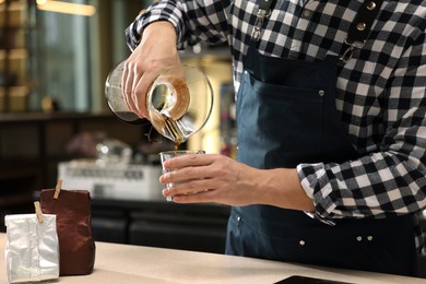 Barista pouring coffee from glass coffeemaker into cup at table in cafe, closeup