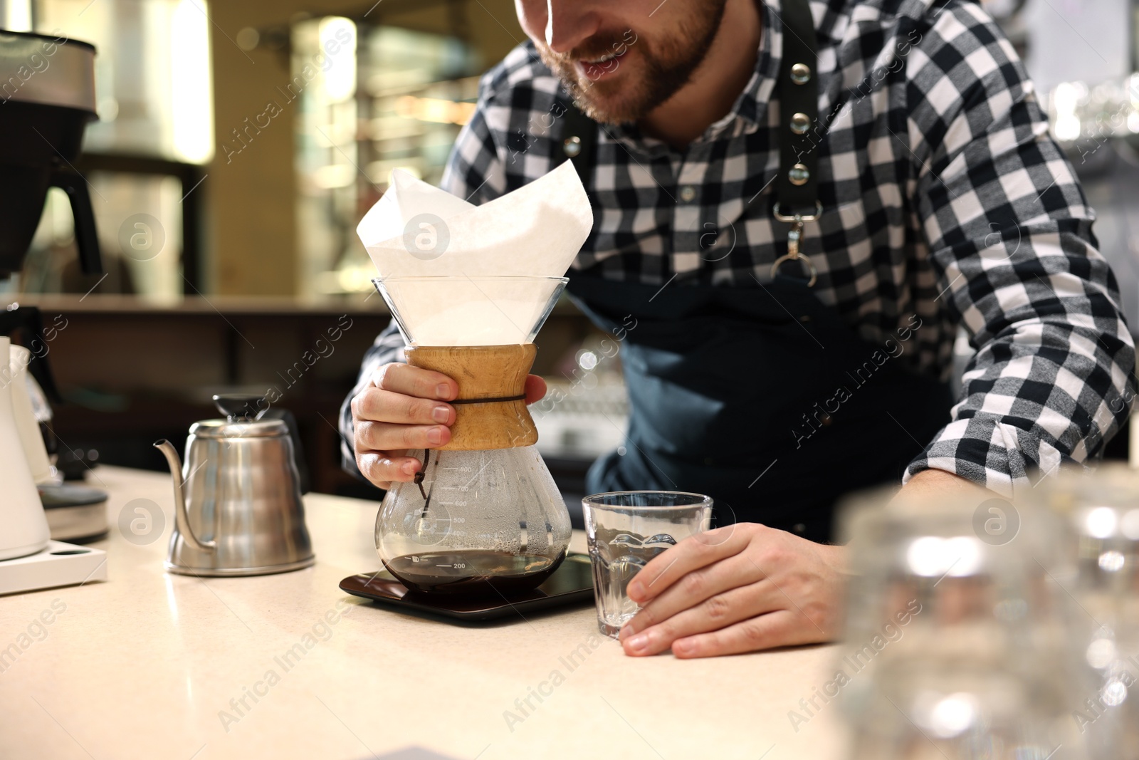 Photo of Barista making coffee with glass coffeemaker at table in cafe, closeup