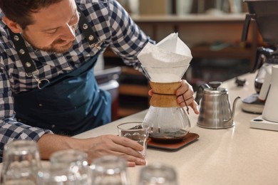 Photo of Barista making coffee with glass coffeemaker at table in cafe, closeup