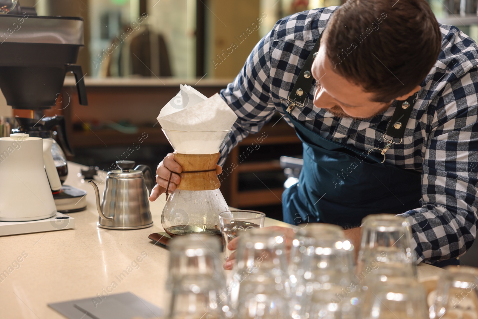 Photo of Barista making coffee with glass coffeemaker at table in cafe