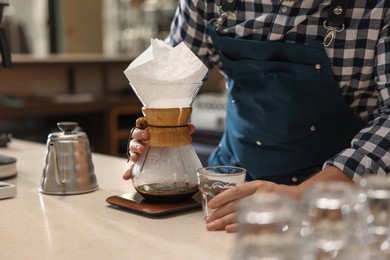 Photo of Barista making coffee with glass coffeemaker at table in cafe, closeup