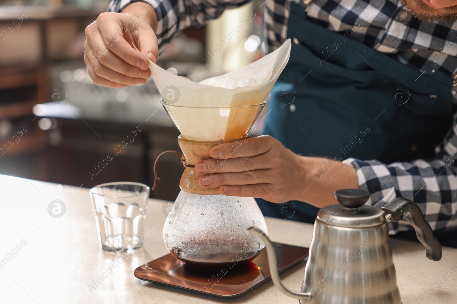 Photo of Barista making coffee with glass coffeemaker at table in cafe, closeup