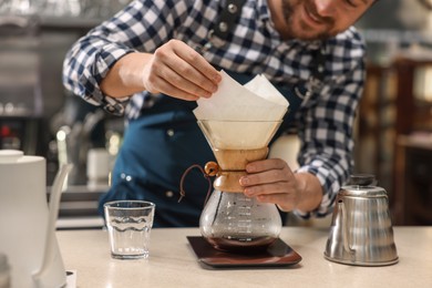 Photo of Barista making coffee with glass coffeemaker at table in cafe, closeup