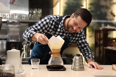 Photo of Barista making coffee with glass coffeemaker at table in cafe