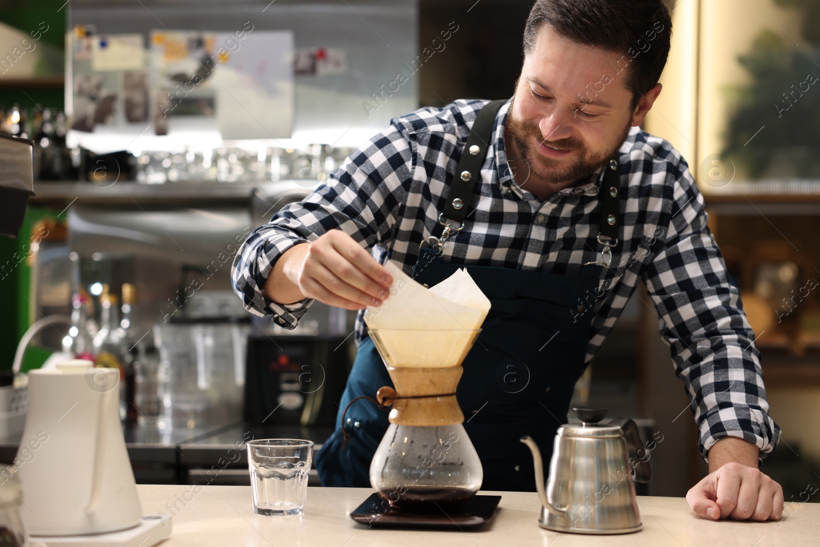 Photo of Barista making coffee with glass coffeemaker at table in cafe