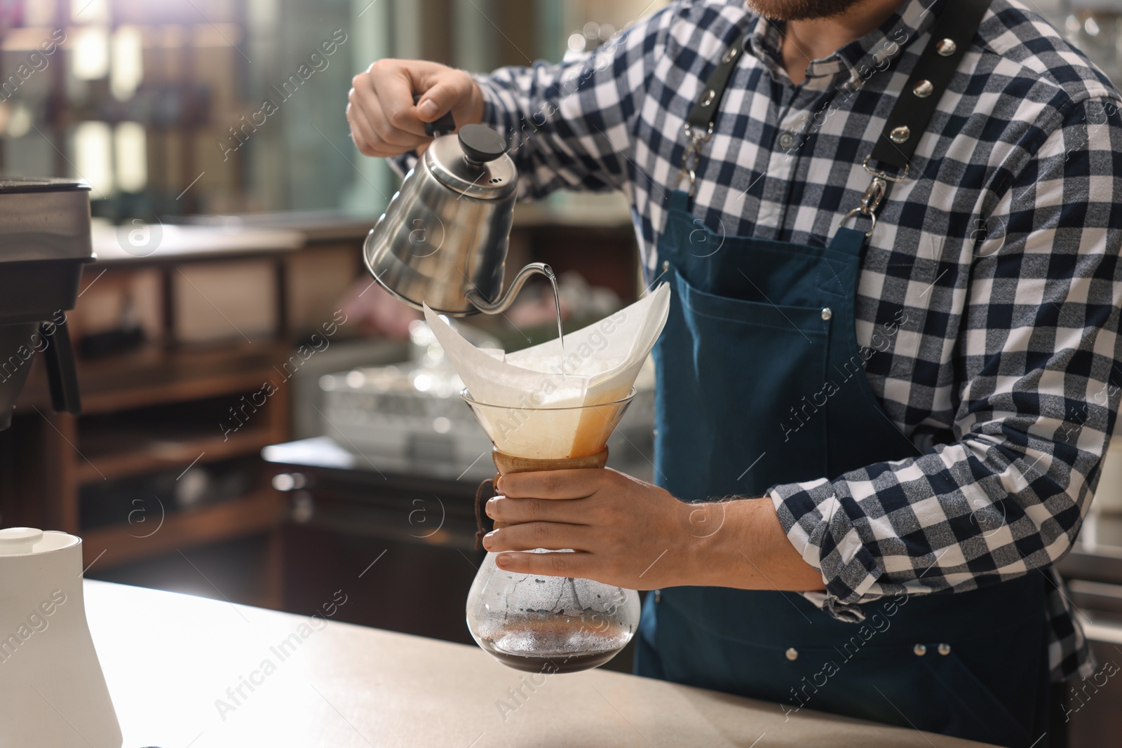 Photo of Barista brewing coffee in glass coffeemaker with paper filter at table in cafe, closeup