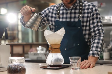 Photo of Barista brewing coffee in glass coffeemaker with paper filter at table in cafe, closeup