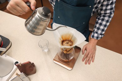 Photo of Barista brewing coffee in glass coffeemaker with paper filter at table in cafe, closeup