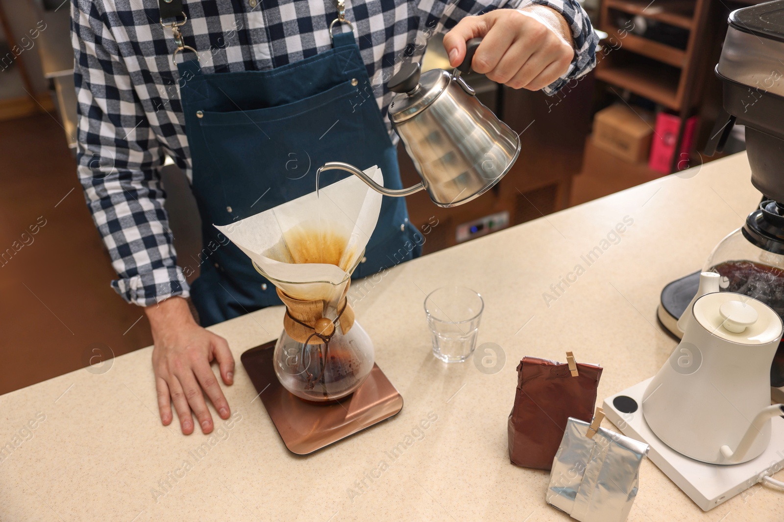 Photo of Barista brewing coffee in glass coffeemaker with paper filter at table in cafe, closeup