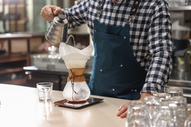 Photo of Barista brewing coffee in glass coffeemaker with paper filter at table in cafe, closeup