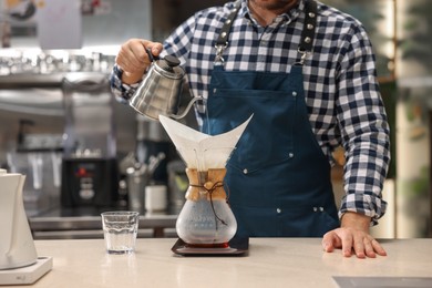 Barista brewing coffee in glass coffeemaker with paper filter at table in cafe, closeup