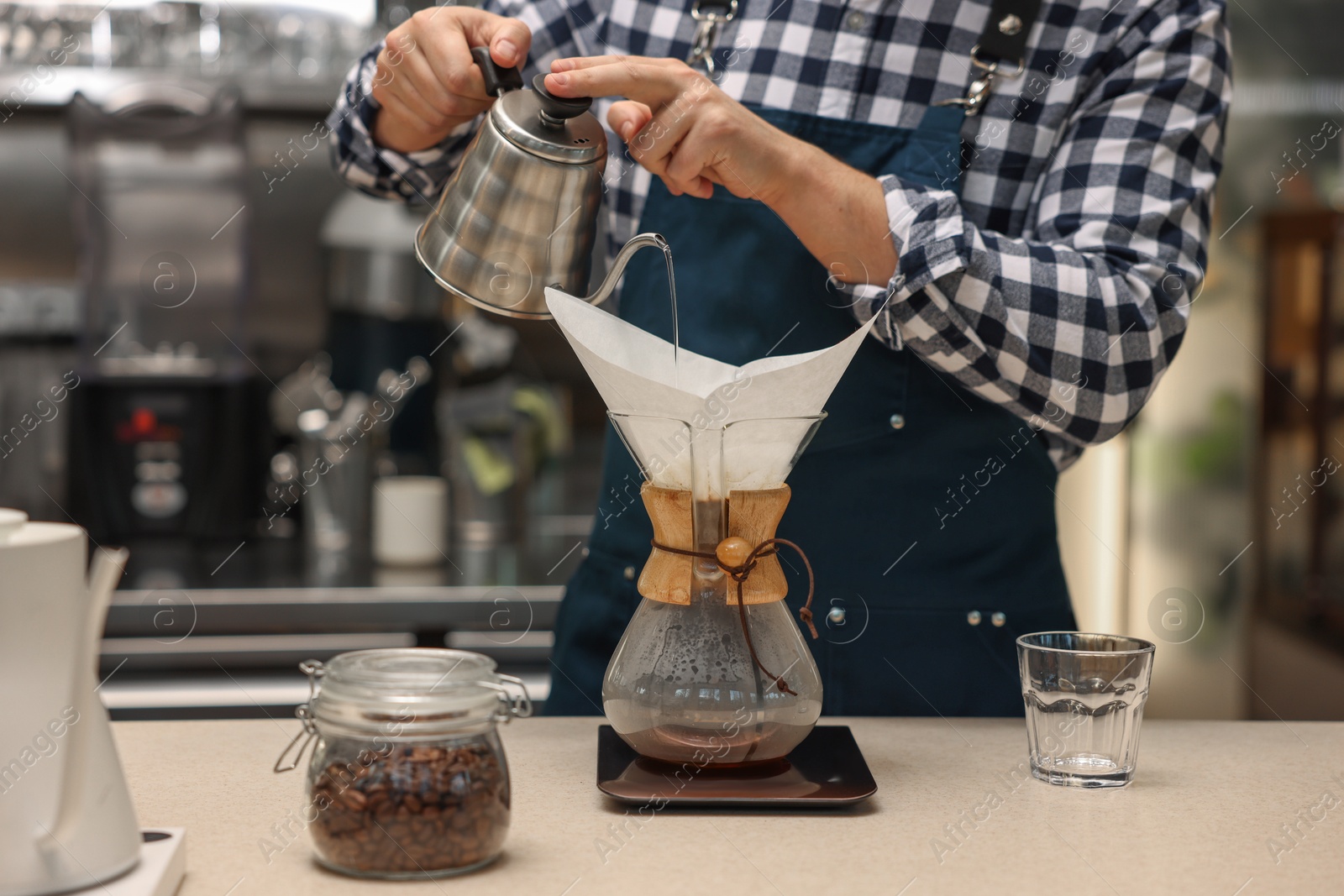 Photo of Barista brewing coffee in glass coffeemaker with paper filter at table in cafe, closeup