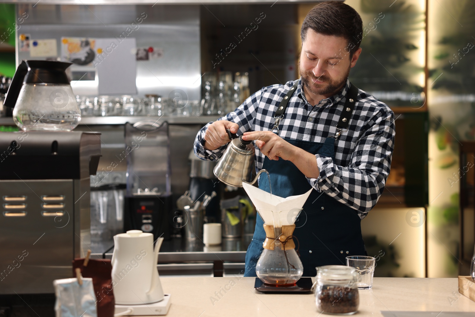 Photo of Barista brewing coffee in glass coffeemaker with paper filter at table in cafe