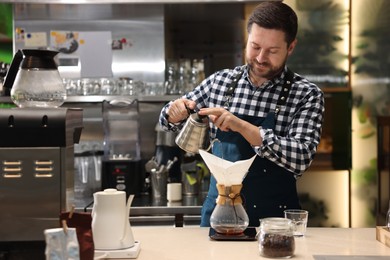 Barista brewing coffee in glass coffeemaker with paper filter at table in cafe