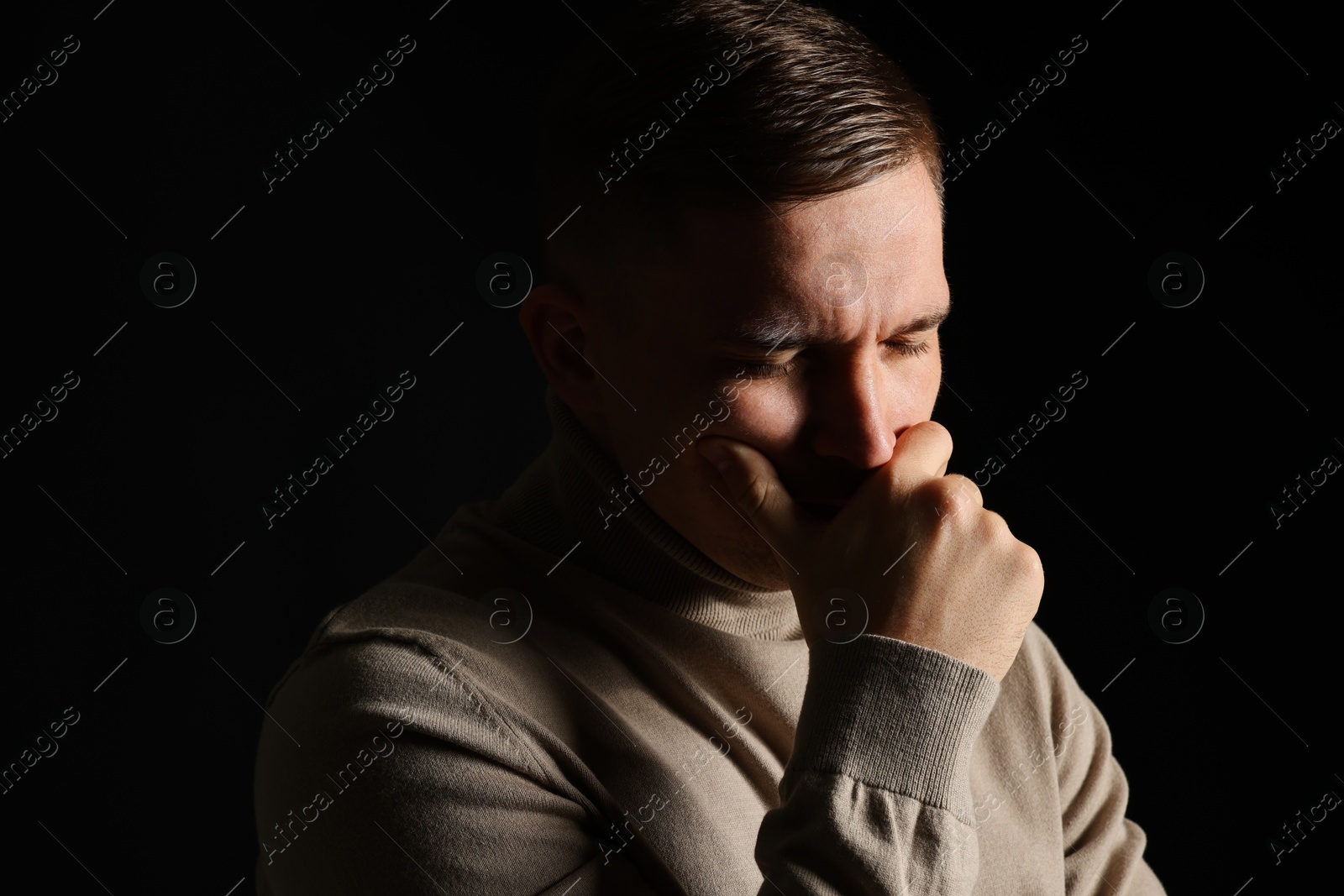 Photo of Distressed young man crying on black background