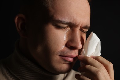 Photo of Crying man wiping tears with tissue on black background, closeup