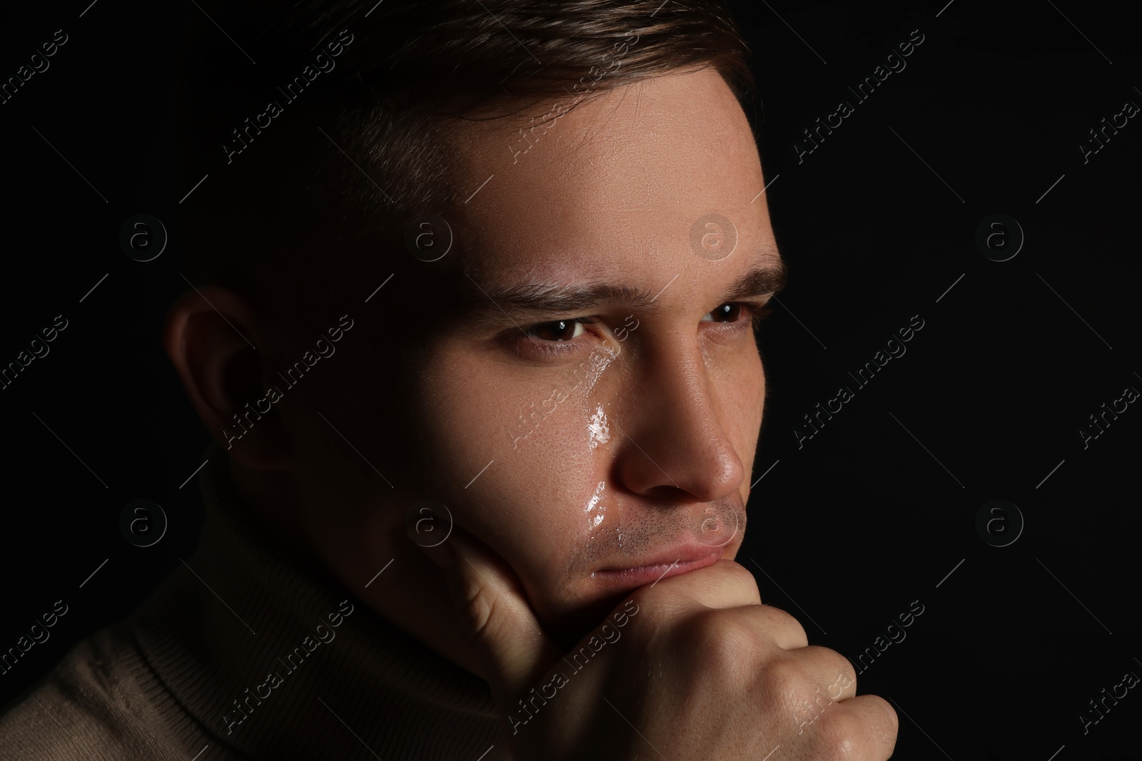 Photo of Distressed young man crying on black background, closeup