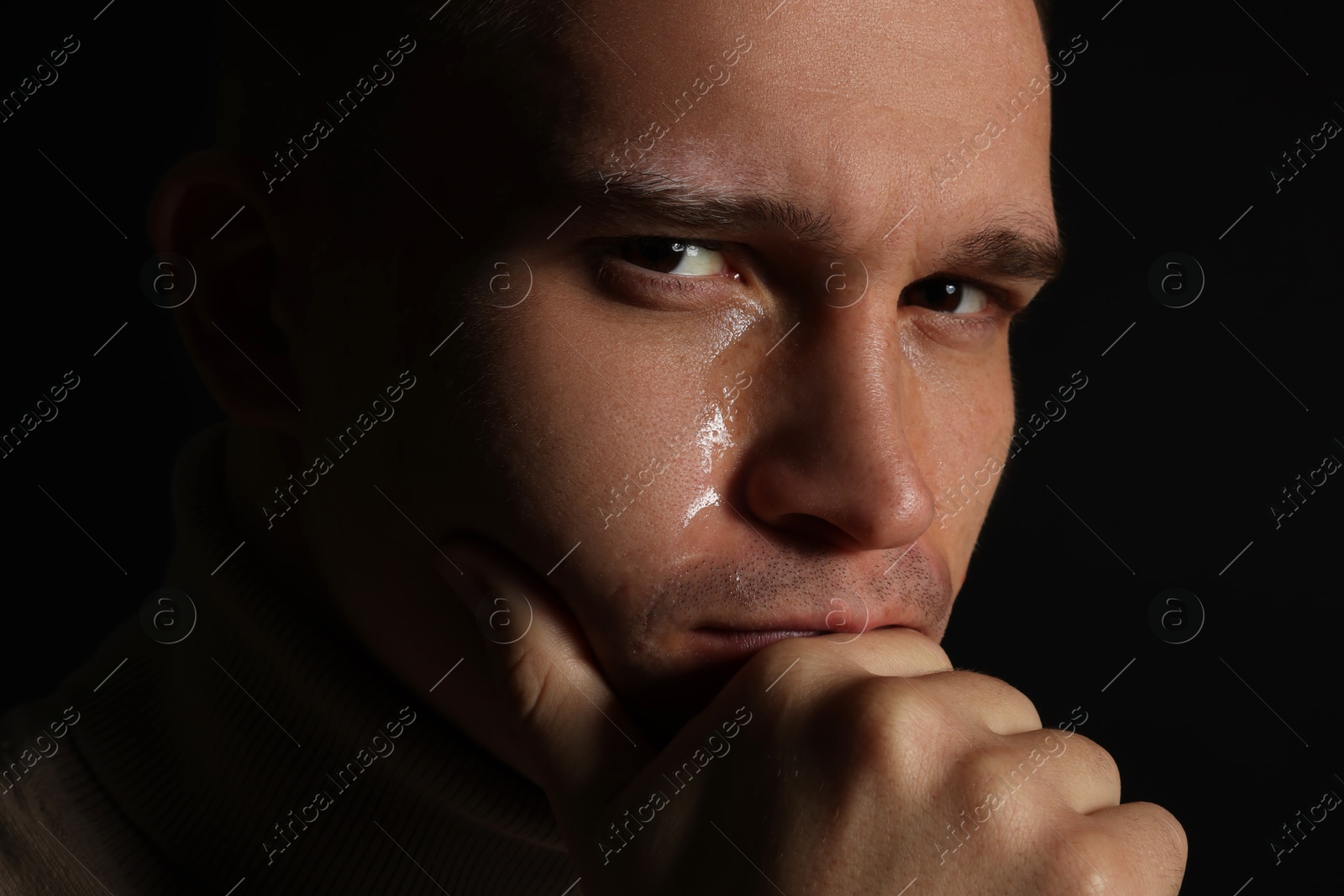 Photo of Distressed young man crying on black background, closeup