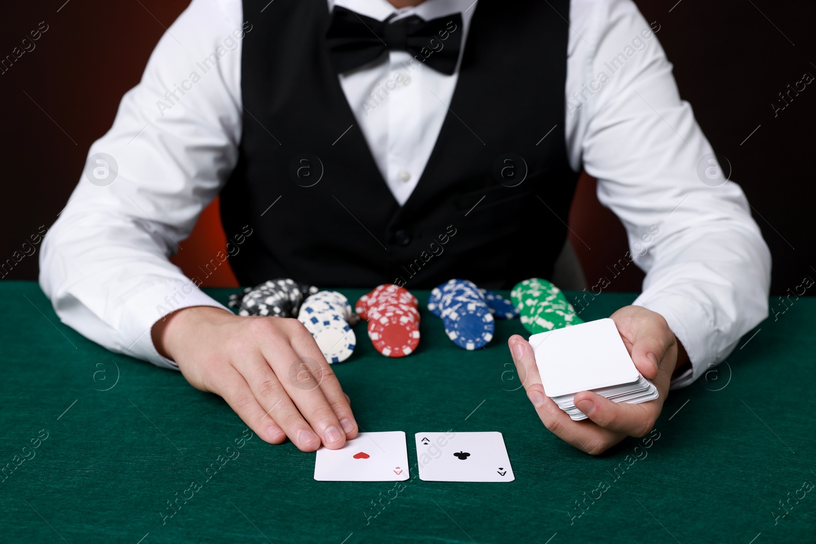 Photo of Professional croupier with playing cards at gambling table, closeup