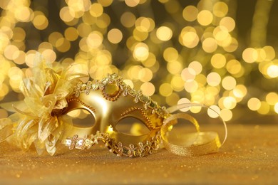 Photo of Beautiful carnival mask on golden shiny surface against blurred lights, closeup