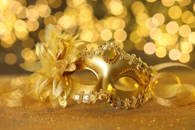 Photo of Beautiful carnival mask on golden shiny surface against blurred lights, closeup