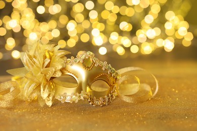 Photo of Beautiful carnival mask on golden shiny surface against blurred lights, space for text