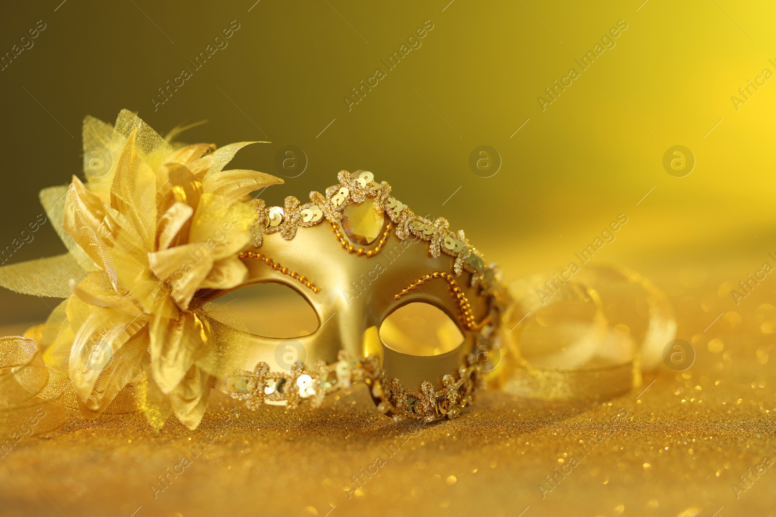 Photo of Beautiful carnival mask on golden shiny surface, closeup