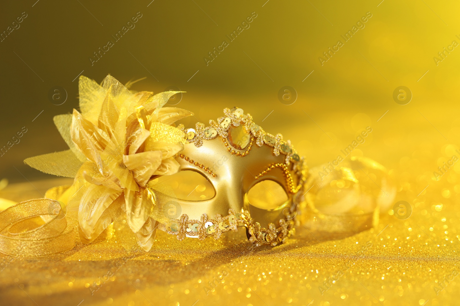 Photo of Beautiful carnival mask on golden shiny surface, closeup