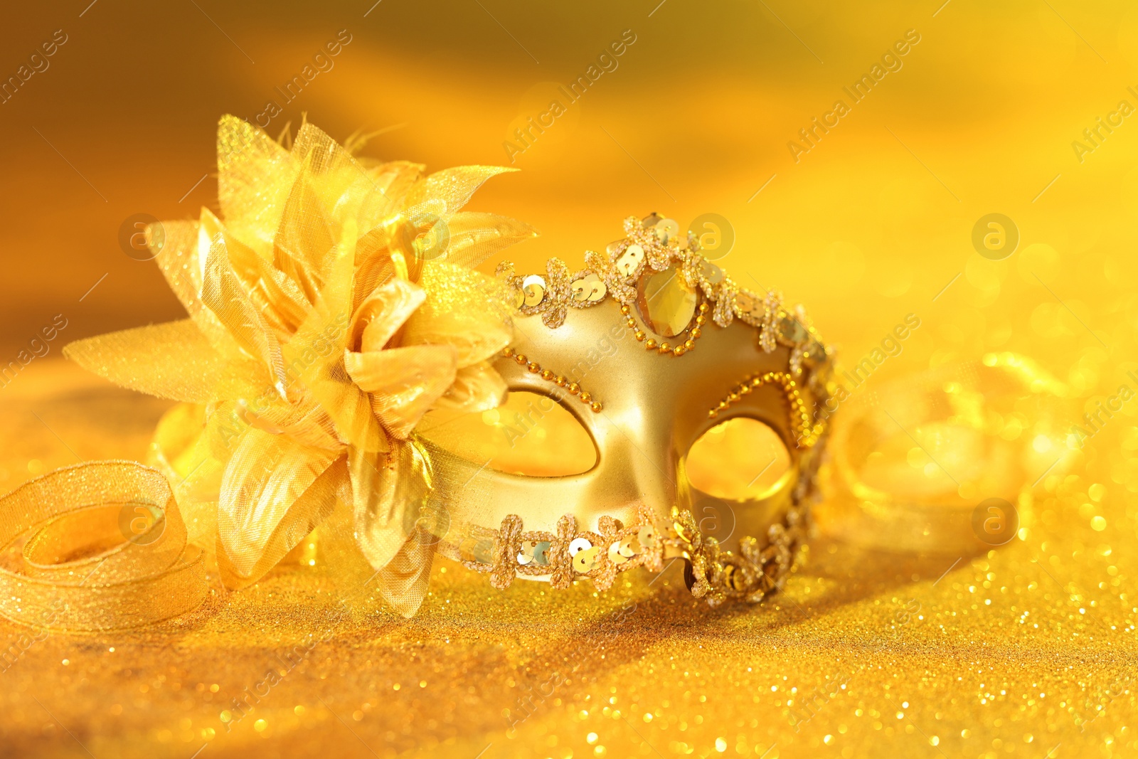 Photo of Beautiful carnival mask on golden shiny surface, closeup