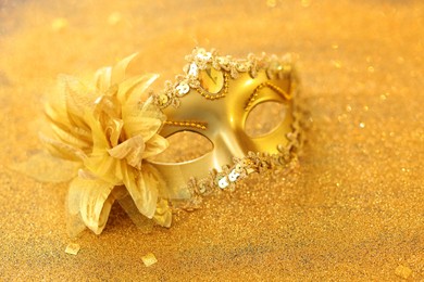 Photo of Beautiful carnival mask on golden shiny surface, closeup