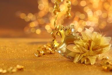 Photo of Beautiful carnival mask on golden shiny surface, closeup. Space for text