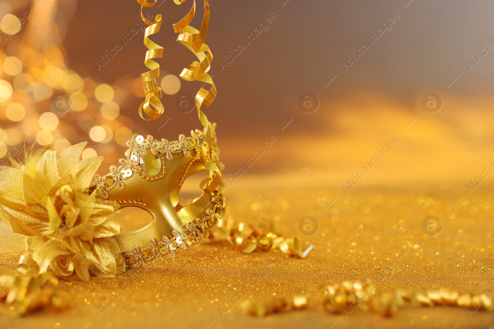 Photo of Beautiful carnival mask on golden shiny surface, closeup. Space for text