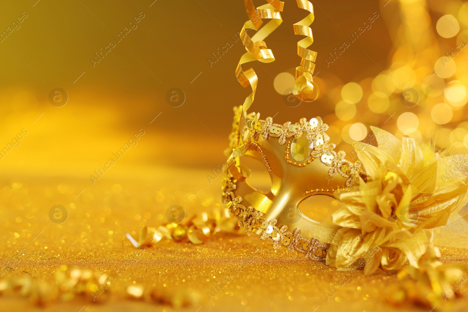 Photo of Beautiful carnival mask on golden shiny surface, closeup. Space for text