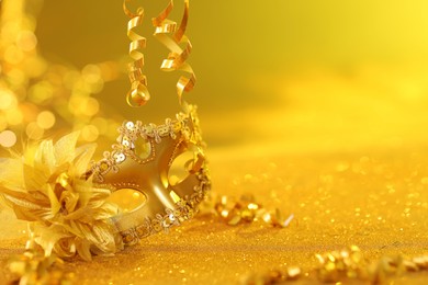 Photo of Beautiful carnival mask on golden shiny surface, closeup. Space for text