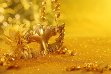 Photo of Beautiful carnival mask on golden shiny surface, closeup. Space for text