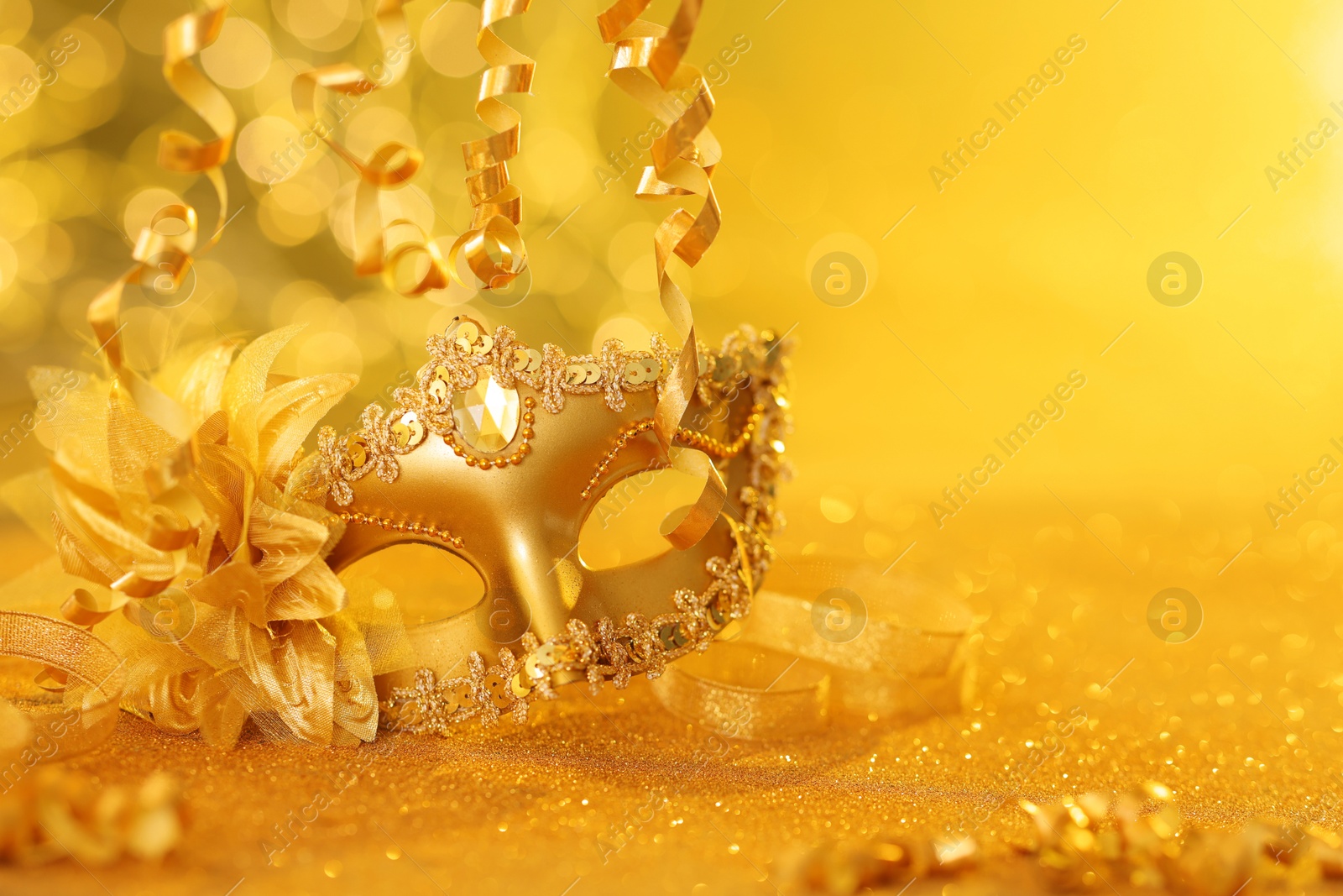 Photo of Beautiful carnival mask on golden shiny surface, closeup. Space for text