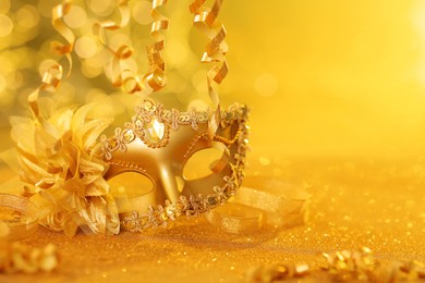 Photo of Beautiful carnival mask on golden shiny surface, closeup. Space for text