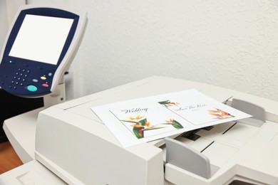 Photo of Modern printer with printed wedding invitation cards indoors, closeup. Printing house